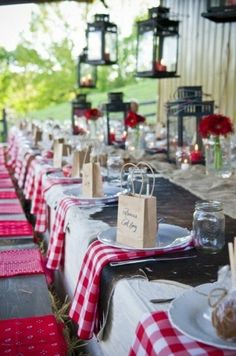 a long table set up with red and white checkered cloths, place settings and candles