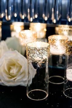 some candles are sitting on a table with white flowers and glass vases in the background