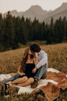 a man and woman sitting on top of a blanket in the middle of a field