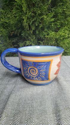 a blue and white coffee cup sitting on top of a table next to a bush