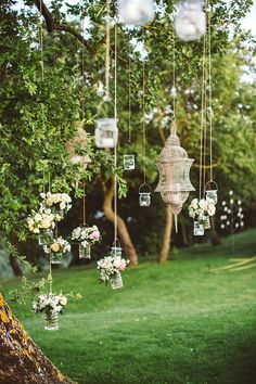 an outdoor wedding with hanging lanterns and flowers in vases on the grass, surrounded by greenery