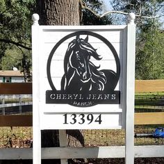 a white sign with a horse on it in front of a fenced area and trees