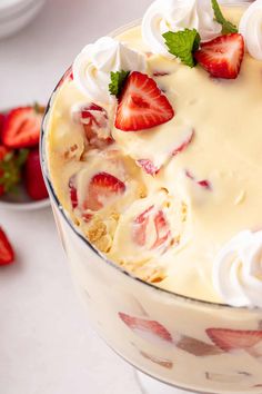 a dessert with strawberries and whipped cream in a glass dish on a white table