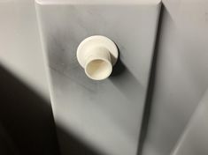 a white cup sitting on the side of a gray wall next to a toilet paper dispenser