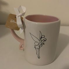 a coffee mug with a tinkerbell on it and a white ribbon around the handle