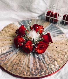 a bouquet of red roses sitting on top of a wooden tray filled with nuts and almonds