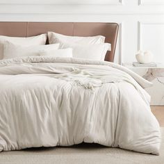 an unmade bed with white linens and pillows on top of the headboard