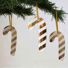 three ornaments hanging from a christmas tree decorated with gold and white striped candy canes