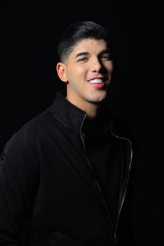 a young man is smiling and wearing a black jacket with zippers on the sleeves