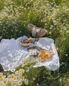 a picnic in the middle of a field full of daisies and oranges is laid out on a blanket