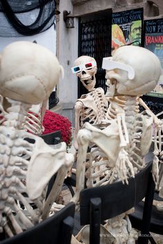 there are three skeletons sitting in the chairs outside with their heads turned to look like they're looking at each other