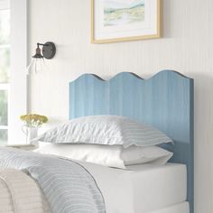 a bed with white pillows and blue headboard next to a painting on the wall