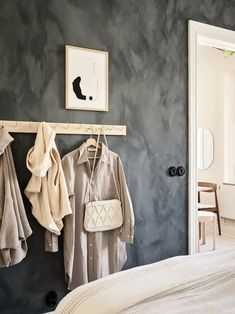 two coats hanging from hooks on a wall next to a bed with a white comforter