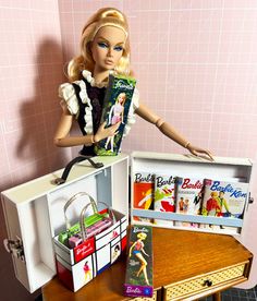 a barbie doll sitting on top of a wooden table next to a suitcase and books