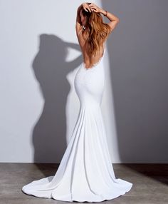 the back of a woman in a white dress with her hands on her head, standing against a wall