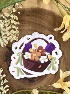 flowers are in a basket on top of a wooden table next to some yellow and white flowers