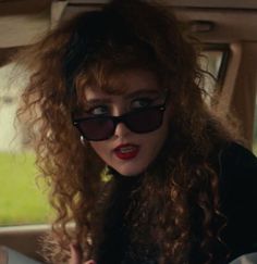 a woman with long curly hair and sunglasses sitting in the back seat of a car