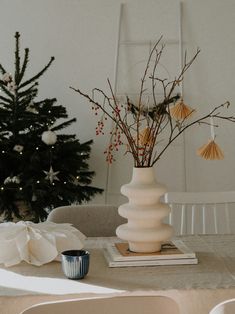 a white vase with some flowers in it on a table next to a christmas tree