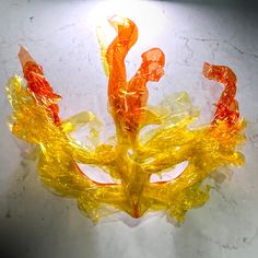 an orange and yellow mask sitting on top of a white table next to a light