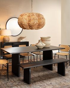 a dining room table with two chairs and a bench in front of it, next to a round mirror on the wall