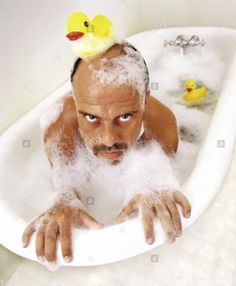 a man with rubber ducks on his head in a bathtub - stock image