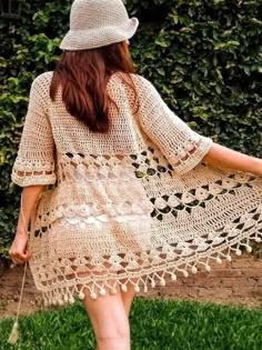 a woman wearing a crochet dress and hat walking in grass with her back to the camera