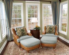 a living room with two wicker chairs and a footstool in front of three windows