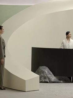 two women are standing in front of a black and white sculpture, one is looking at another woman