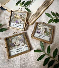 three framed pictures sitting on top of a table next to some leaves and an open book