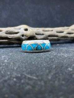 a ring with blue and white designs sitting on top of a gray surface next to a piece of driftwood