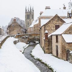 a small river running through a snow covered village next to tall brick buildings with spires on top