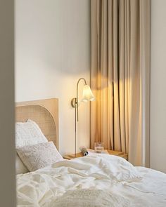 an unmade bed with white linens and a lamp next to it in a bedroom