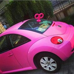 a pink car is parked on the side of the street with a bow on top