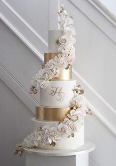 a three tiered wedding cake with white and gold flowers on the top, sitting on a pedestal