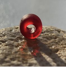 a red donut sitting on top of a cement slab with water droplets around it