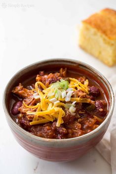 a bowl filled with chili and cheese next to a piece of bread