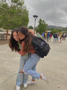 two girls hugging each other in front of a group of people on a cloudy day