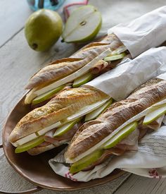 several sandwiches are on a plate with apples in the background and napkins wrapped around them