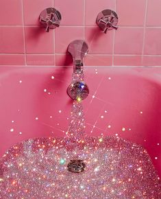 a pink bathtub filled with lots of shiny beads and water running from the faucet