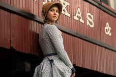 a woman in a dress and hat leaning against a red building with the words texas on it