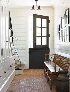 a wooden bench sitting in front of a door next to a white wall with pictures on it