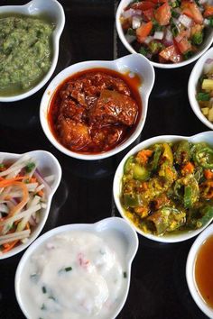 several bowls filled with different types of food on top of a black tray, including vegetables and sauces