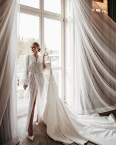 a woman standing in front of a window wearing a white robe and high heeled shoes