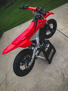 a red dirt bike parked on top of a cement slab in front of some grass