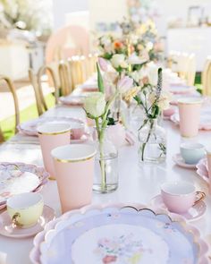 the table is set with pink and white dishes, cups, and flowers in vases