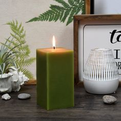 a green candle sitting on top of a wooden table next to rocks and potted plants