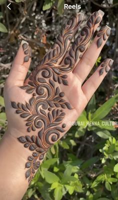 someone is holding their hand with henna designs on it, and there are green leaves in the background