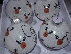 three white christmas ornaments in a box with reindeer designs on the top and bottom one has a red nose