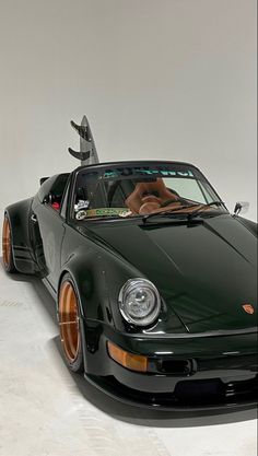 a green sports car parked in a white room with its hood up and the top down