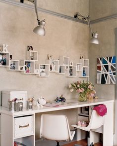 a white desk topped with lots of pictures and vase filled with flowers next to a chair